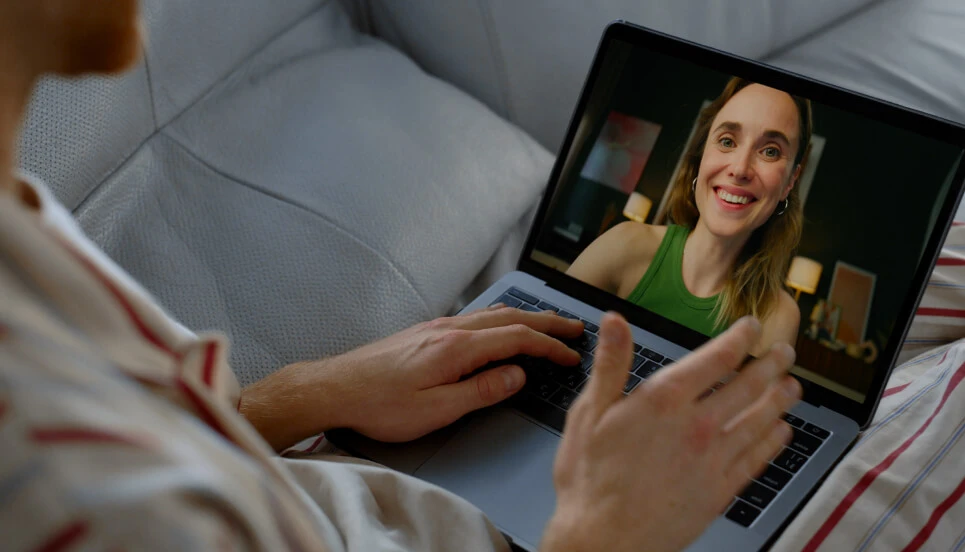 Person on a couch video chatting with a woman on a laptop screen.