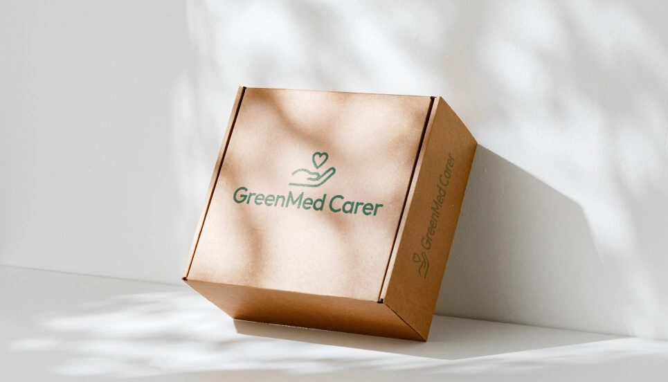 A brown cardboard box with the logo "GreenMed Carer" on it, placed against a light background with leaf shadows.