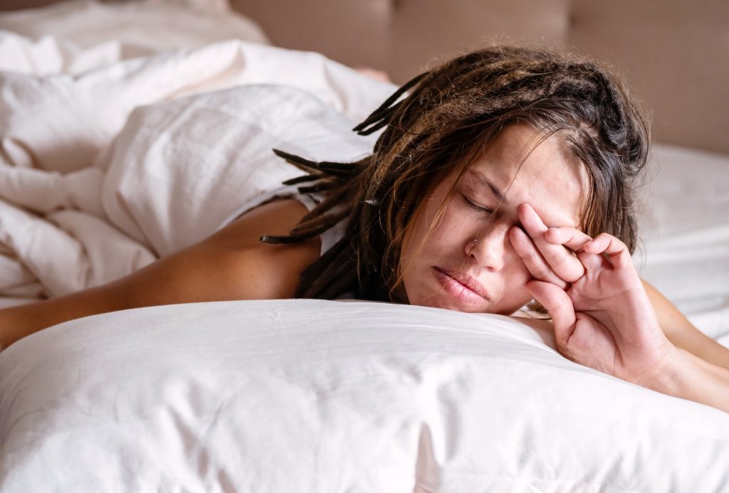 Person lying in bed on their stomach, appearing sleepy, with a hand resting near their face, reflecting on lifestyle changes and how small adjustments can make a difference.